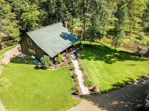 A two-story house with a green roof, surrounded by a well-maintained lawn and trees. - Secluded Cabin on a mountain stream on 7.5 acres (Lenoir)