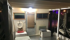 Ein kleiner, gut beleuchteter Raum mit einem Bett, einer Sitzecke, einem Fenster mit Blick und einer Tür zu einem weiteren Zimmer.