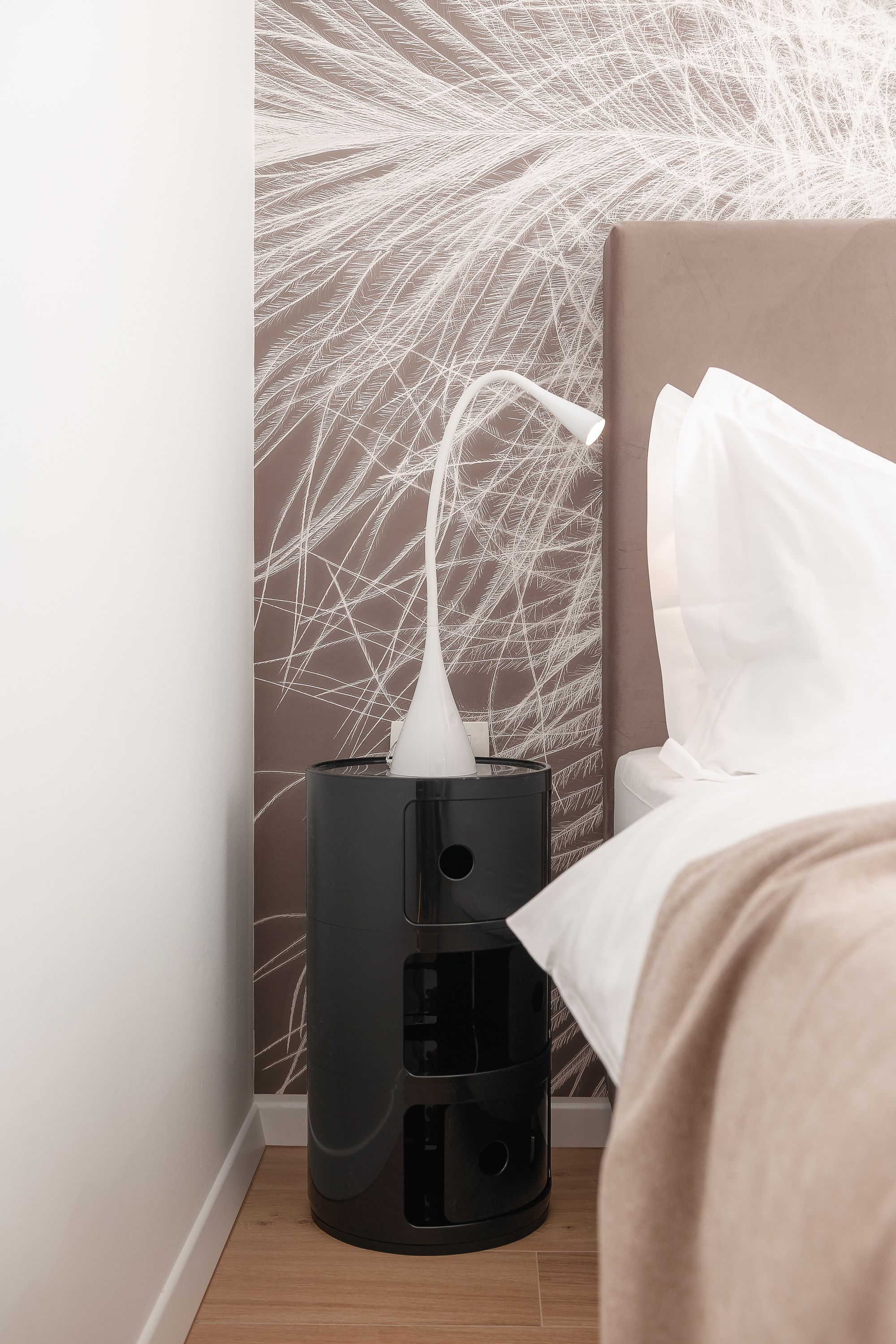 A modern hotel room with a bed, a bedside table, and a wall with a unique abstract design.