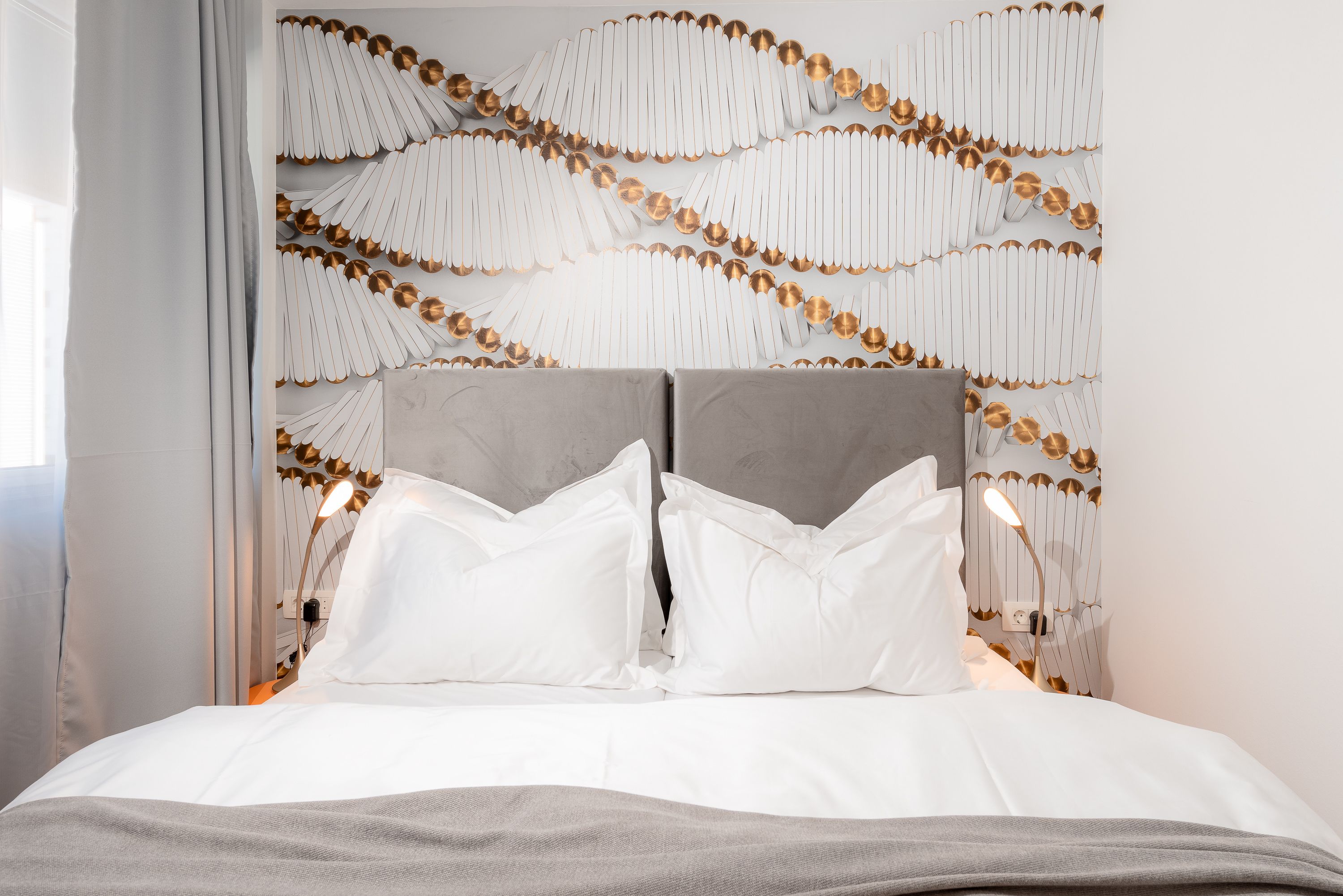 A modern bedroom with a grey headboard, white bedding, and a decorative wall panel.