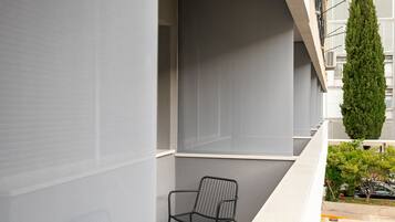 Un balcon avec une chaise en métal, un grand arbre vert et la façade d’un immeuble.