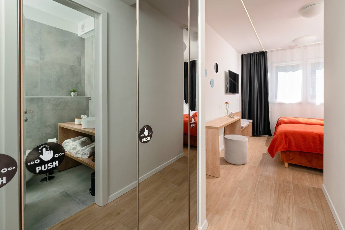 Quarto de hotel moderno com chuveiro, cama, escrivaninha e espelho.