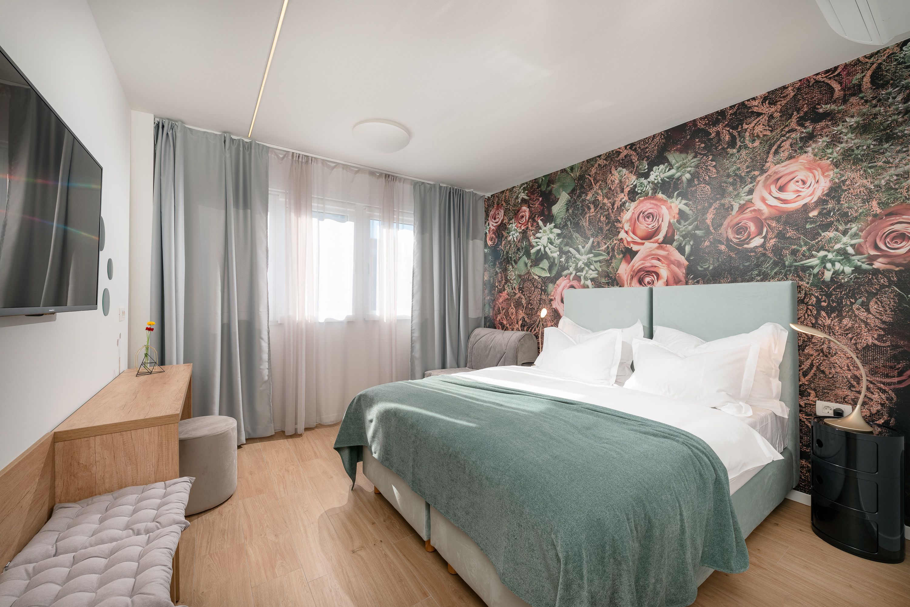 Un dormitorio moderno con cama, mesita de noche, televisor y papel tapiz floral.