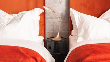 A bed with white and red bedding, a black nightstand with a lamp, and a grey wall.