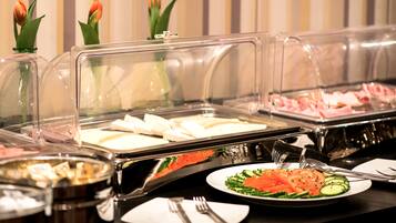 A buffet setup with various food items under protective covers, including salads and meats.