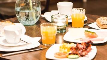 A breakfast setting with a glass of orange juice, a cup, a plate with eggs and bacon, and a water bottle.