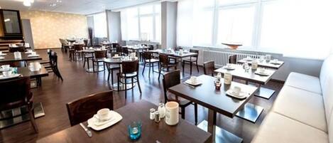 A spacious dining area with multiple tables and chairs, large windows providing natural light, and a modern interior design.