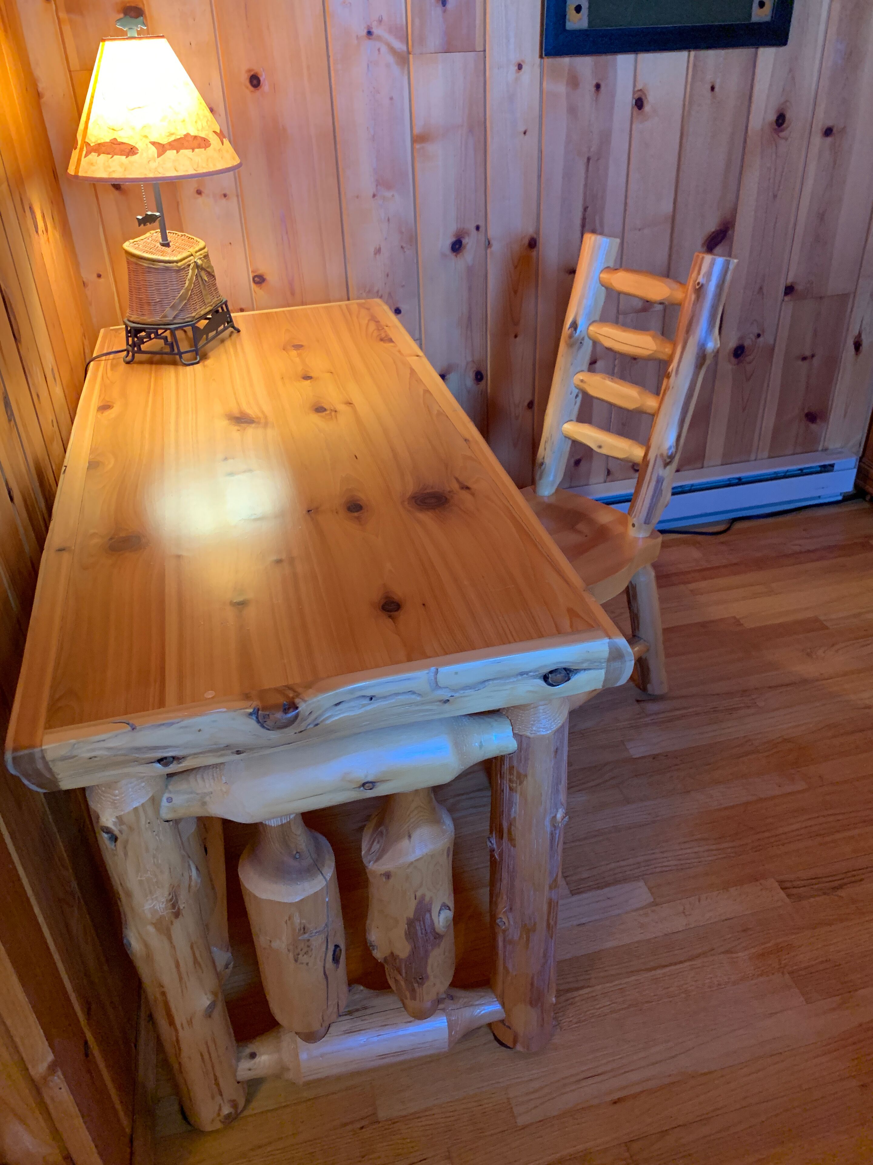 A wooden dining table with a lamp on it, set against a wooden wall.