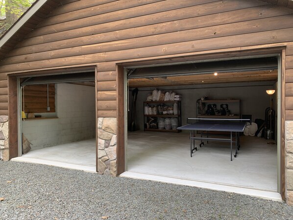 A log cabin with two open garage doors leading to a covered area with a ping pong table.