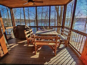 A covered outdoor area with a wooden table and chairs, a grill, and a view of a snowy landscape through large windows.
