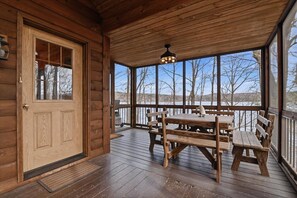 A wooden cabin with a covered porch, a wooden table and benches, and a view of trees and hills.