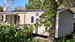 Une maison mobile dotée d’une véranda, d’un espace extérieur couvert aménagé en coin salon et d’un petit abri de jardin.