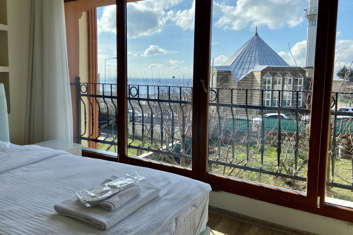 A hotel room with a large window offering a view of a building with a pointed roof and a fence in the foreground.