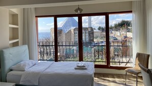 A hotel room with a bed, a chair, and a large window offering a view of buildings and a body of water. - Doga Villa Guesthouse (Istanbul)