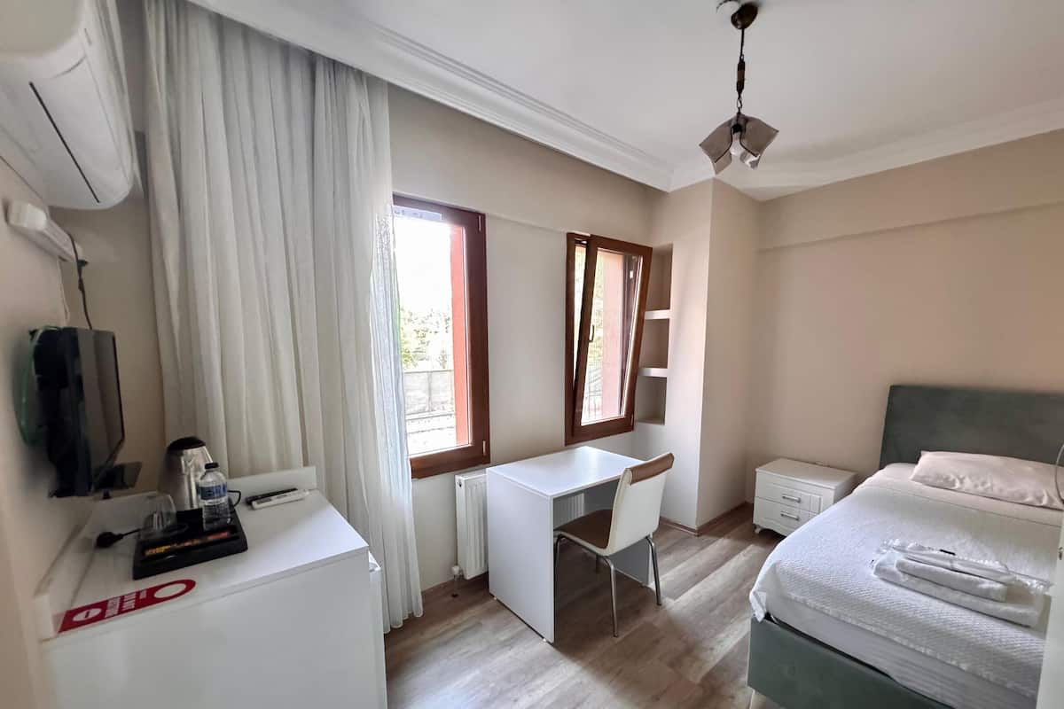 A hotel room with a bed, a desk, a chair, a TV, a radiator, and a window with curtains.