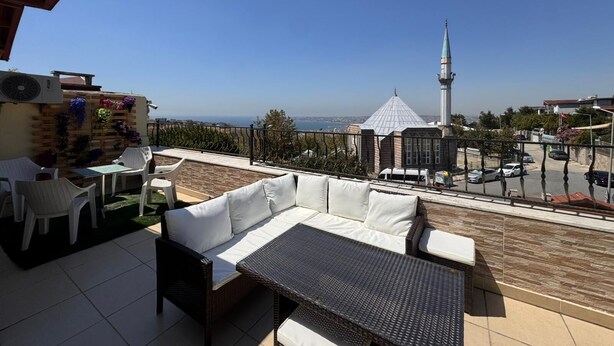 A rooftop terrace with outdoor seating, a view of a mosque with a minaret, and a clear sky. - Doga Villa Guesthouse (Istanbul)