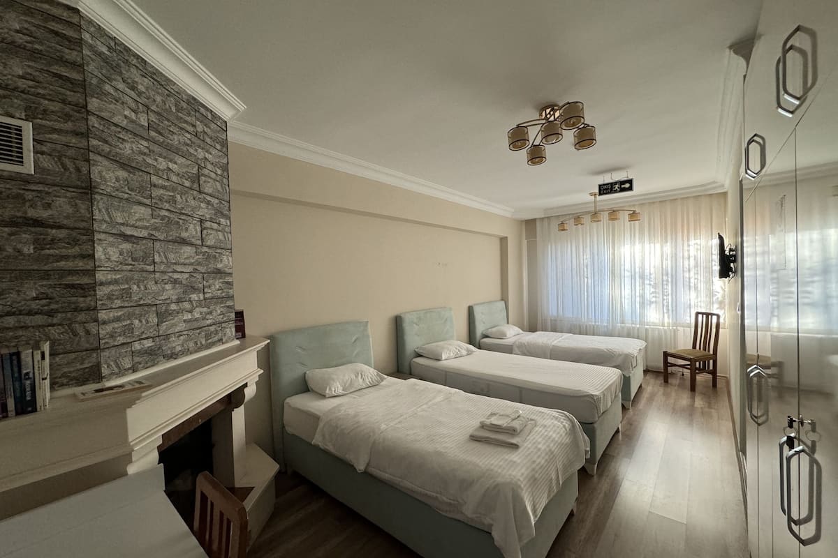 A hotel room with three beds, a stone wall, a fireplace, and a modern chandelier.