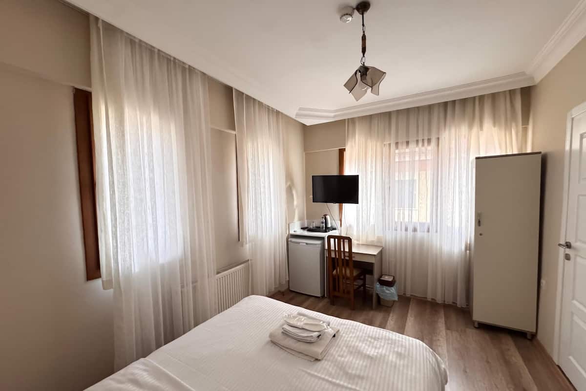A hotel room with a bed, a desk with a computer, a television, and a wardrobe.