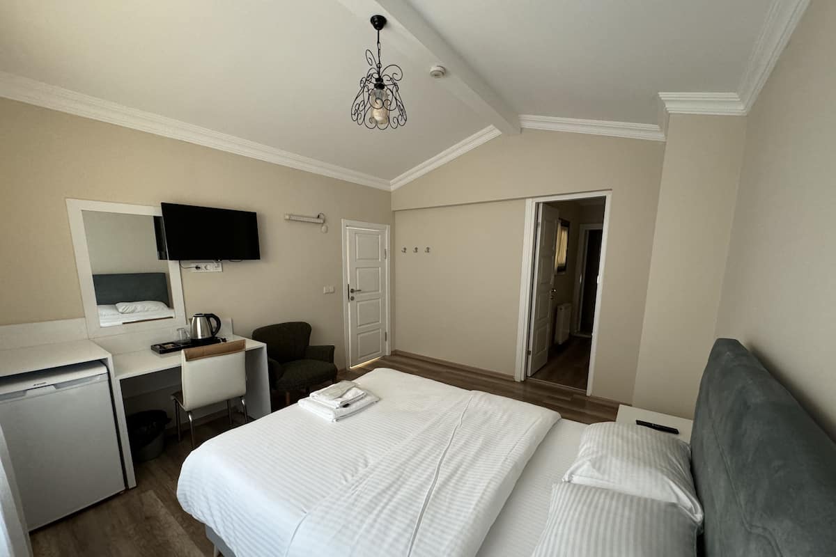 A hotel room with a bed, desk, chair, television, and a door leading to another room.