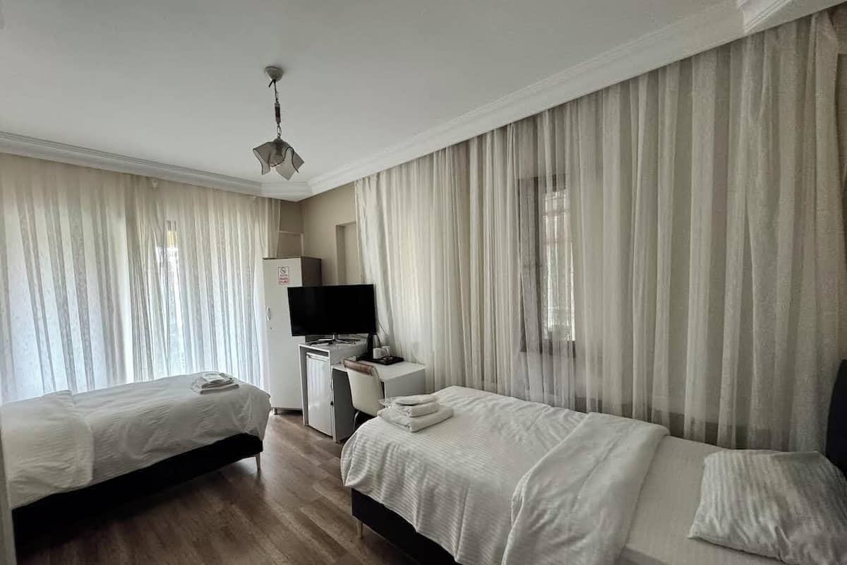 A hotel room with two beds, a desk with a television, and sheer curtains.