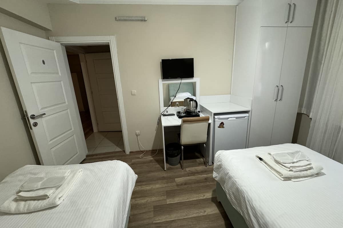 A hotel room with two beds, a desk with a computer, a small refrigerator, and a wardrobe.