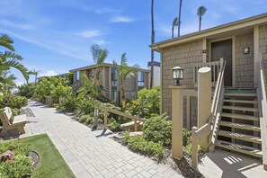 A pathway leading to a building with a number sign, surrounded by greenery and palm trees. - Beachfront-Full Panoramic Ocean Views. D24 North Coast Village (Oceanside)
