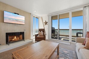 Un salon doté d’une cheminée, d’un téléviseur à écran plat, d’un canapé et d’un balcon aménagé avec du mobilier d’extérieur.