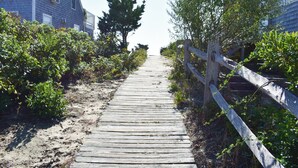 A wooden pathway leading to a beach area, flanked by vegetation and a wooden fence. - Seven bedroom directly across street from shared/private beach (Dennis Port)