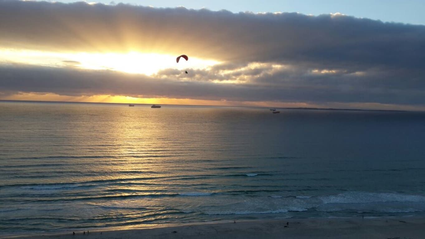 Une plage au coucher du soleil, avec une mer calme et une personne pratiquant le parapente.