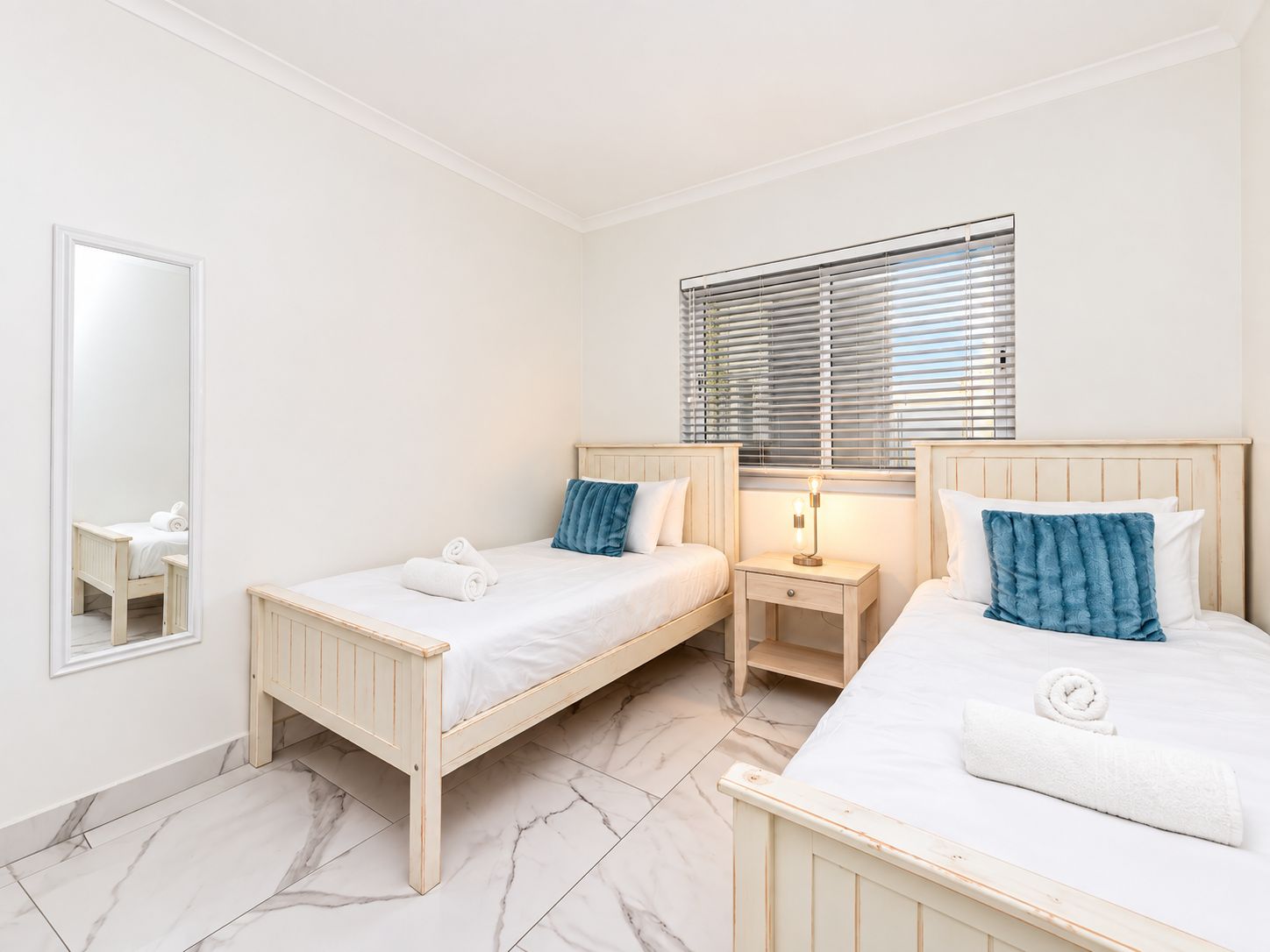 Een hotelkamer met twee bedden, een nachtkastje, een spiegel en een raam met zonwering.