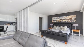 Ein modernes Schlafzimmer mit einem großen Bett, einer Couch, einem Essbereich und einer Küche im Hintergrund.