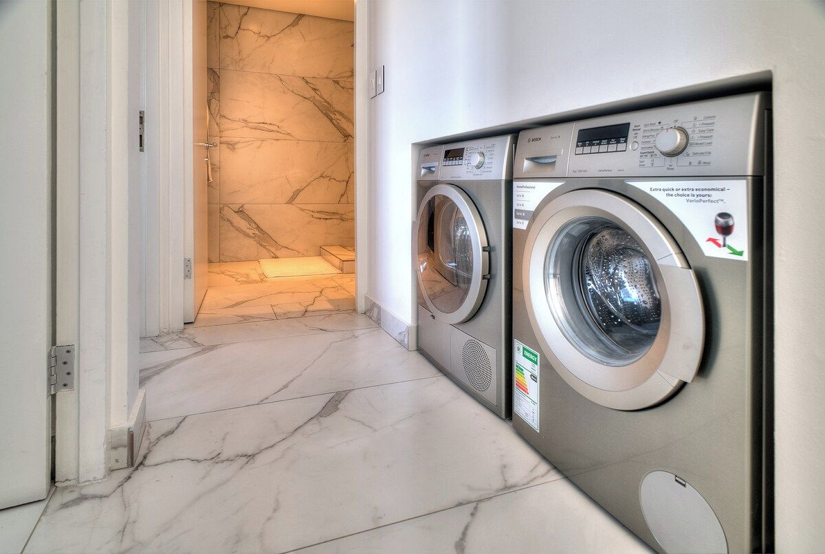 A laundry area with two Bosch washing machines, a marble-tiled floor, and a white door.