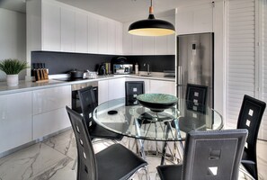 Une cuisine moderne avec une table à manger en verre, des chaises noires et des appareils électroménagers en acier inoxydable.