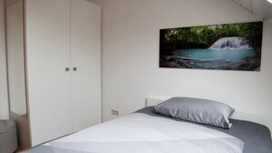 Une chambre à coucher avec un lit, un oreiller gris, une couette blanche, une armoire et un tableau représentant une cascade.