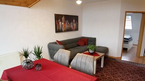 Un salon avec une table rouge, un canapé gris et un tableau représentant un paysage urbain.
