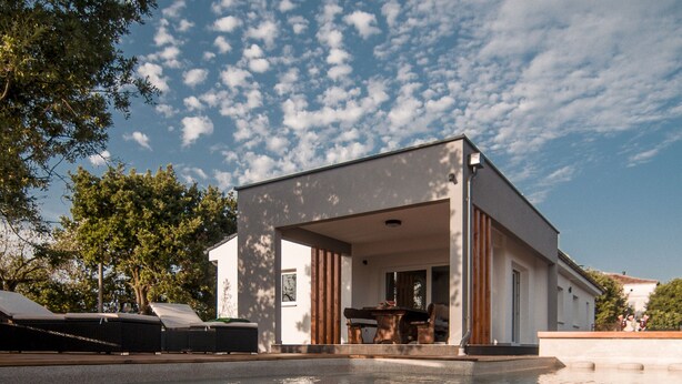 A modern house with a pool, featuring a covered outdoor area with a table and chairs.