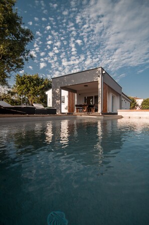Una casa moderna con piscina, que cuenta con un espacio exterior cubierto con mesa y sillas.