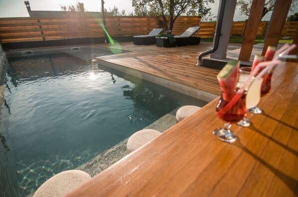 Une terrasse en bois avec une piscine, des chaises longues et un coin bar où l’on sert des boissons.