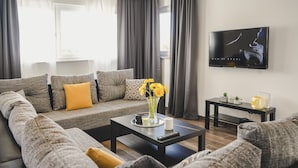 A modern living room with a grey sectional sofa, a coffee table, a TV on the wall, and a window with curtains.