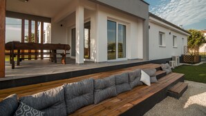 A modern outdoor seating area with wooden benches and cushions, a covered patio, and large windows.