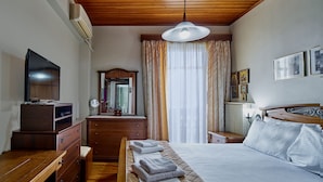 Ett hotellrum med en säng i trä, en tv-apparat på en byrå, en spegel och ett fönster med gardiner.