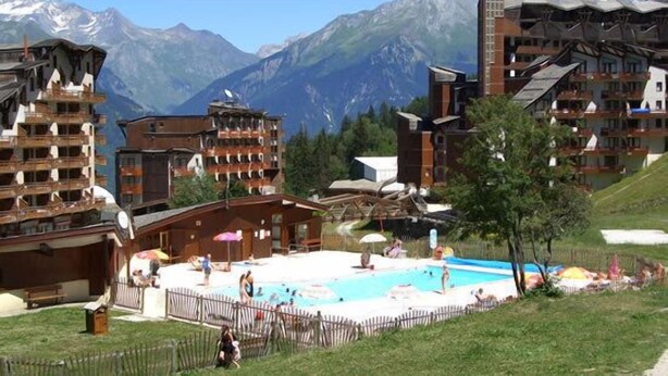 Un resort con área de piscina rodeada de edificios, con montañas al fondo.