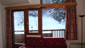 Una habitación acogedora con un banco de madera y una mesa, ventanas amplias con cortinas, y vistas a un paisaje nevado.