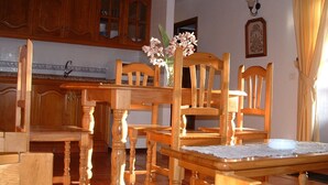 A wooden dining table with chairs, a vase with flowers, and a kitchen area with wooden cabinets and a sink. - Casa los Viñedos (A) with views of the sea, the mountains and the volcanoes. (Fuencaliente de la Palma)