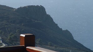 A mountainous landscape with a prominent cliff and a road winding down towards the sea. - Casa los Viñedos (A) with views of the sea, the mountains and the volcanoes. (Fuencaliente de la Palma)