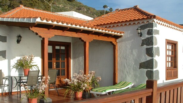 A coastal building with a tiled roof, a stone wall, and a wooden deck with lounge chairs and potted plants. - Casa los Viñedos (A) with views of the sea, the mountains and the volcanoes. (Fuencaliente de la Palma)