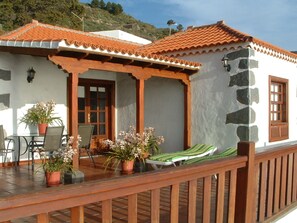 A coastal building with a tiled roof, a stone wall, and a wooden deck with lounge chairs and potted plants. - Casa los Viñedos (A) with views of the sea, the mountains and the volcanoes. (Fuencaliente de la Palma)