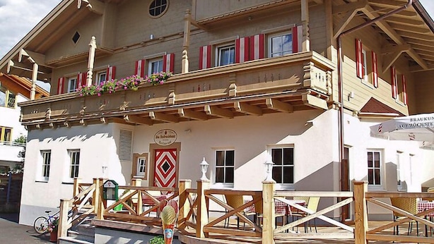 Un bâtiment de style alpin traditionnel, doté d’un balcon, de balustrades en bois et de volets rouges.