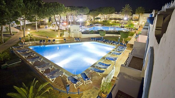 Una piscina con tumbonas y vistas del complejo turístico de noche.