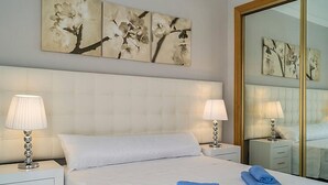 Habitación de hotel con una cama grande, dos mesitas de noche con lámparas, un espejo y obras de arte en las paredes.